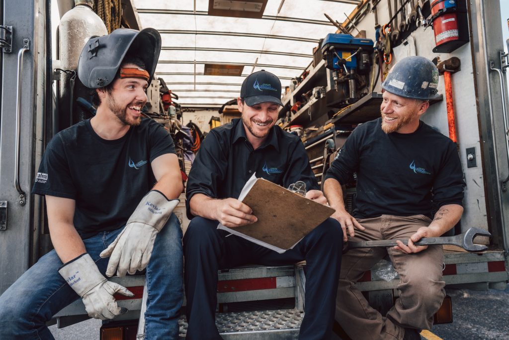 Trois techniciens de Plomberie St-Jovite souriants en pause à l'arrière d'un camion de service rempli d'outils.