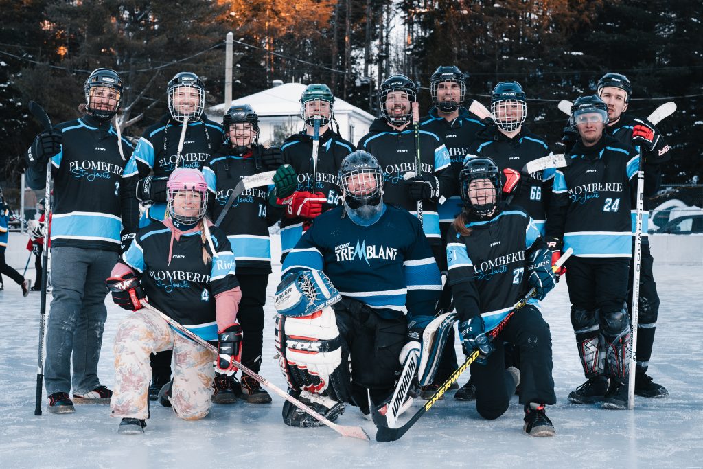 L'équipe de hockey de Plomberie St-Jovite, incluant les joueurs et le gardien de but, pose fièrement en maillots sur une patinoire extérieure.