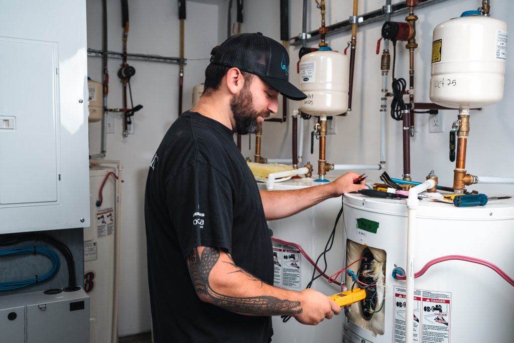 Technicien vérifiant un chauffe-eau avec un multimètre.